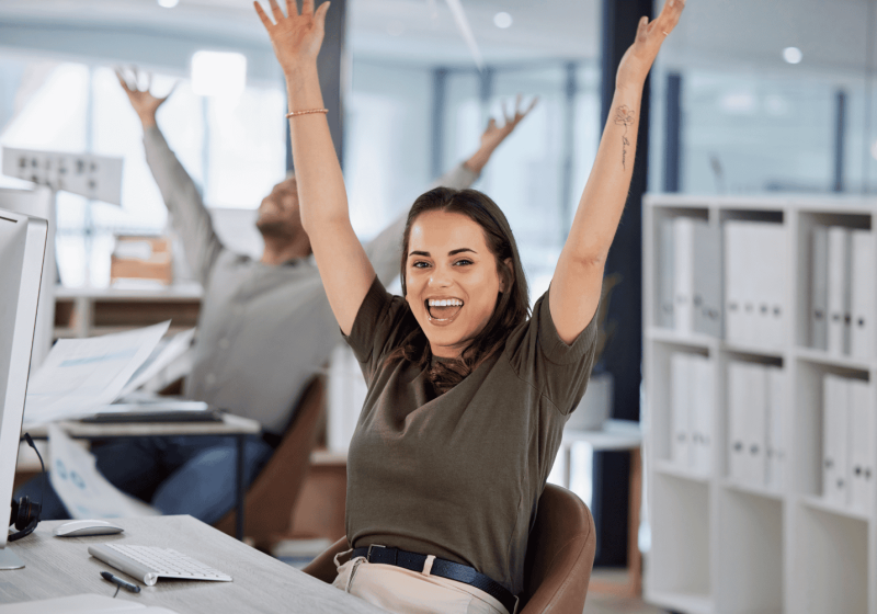 a woman sitting at her desk with her arms up celebrating work boundaries